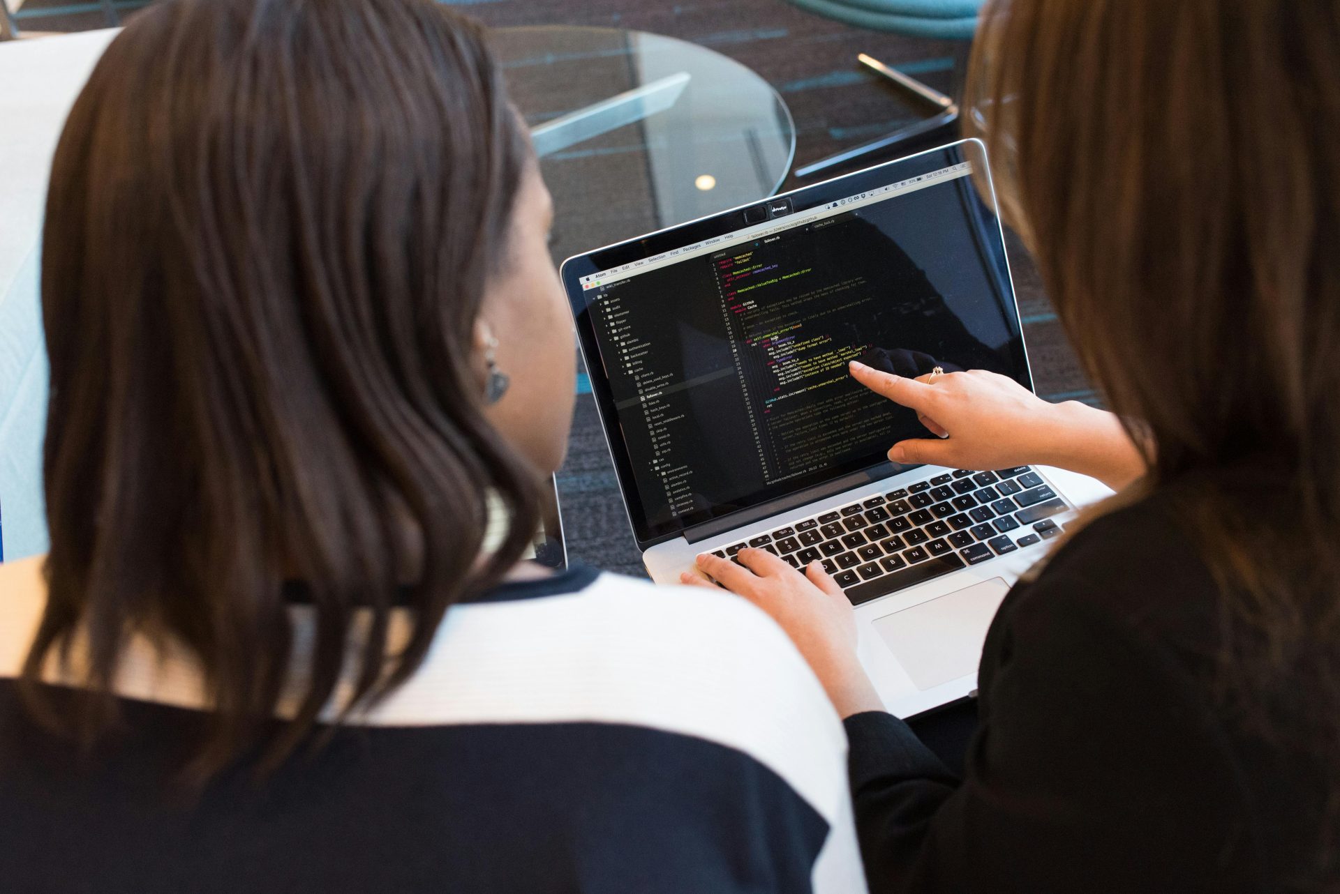 Zwei Frauen arbeiten gemeinsam an der Softwareprogrammierung in einem Innenraum und konzentrieren sich dabei auf den Code.