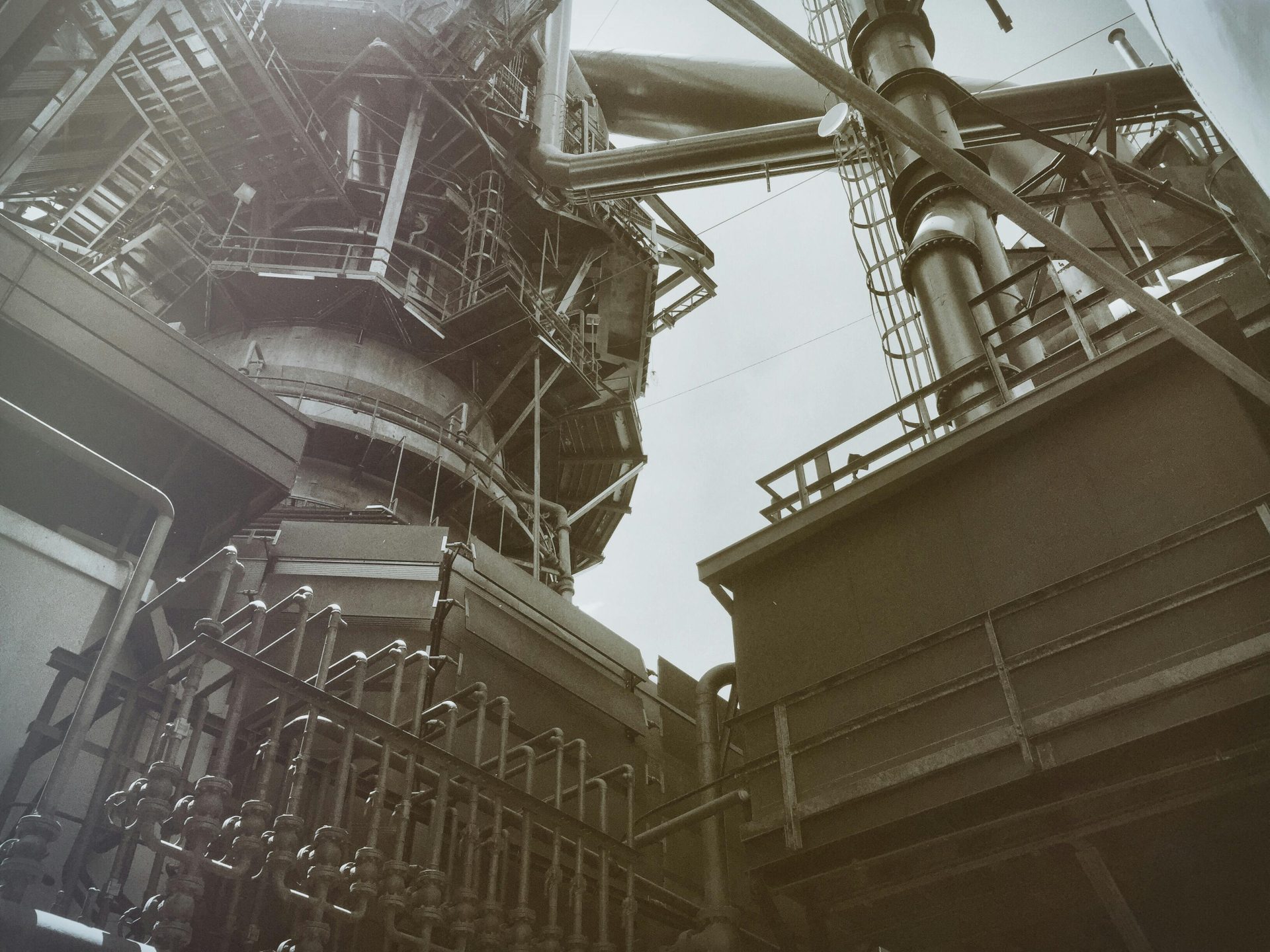 Blick aus der Froschperspektive auf industrielle Stahlkonstruktionen und Rohre, die moderne Ingenieurskunst veranschaulichen.