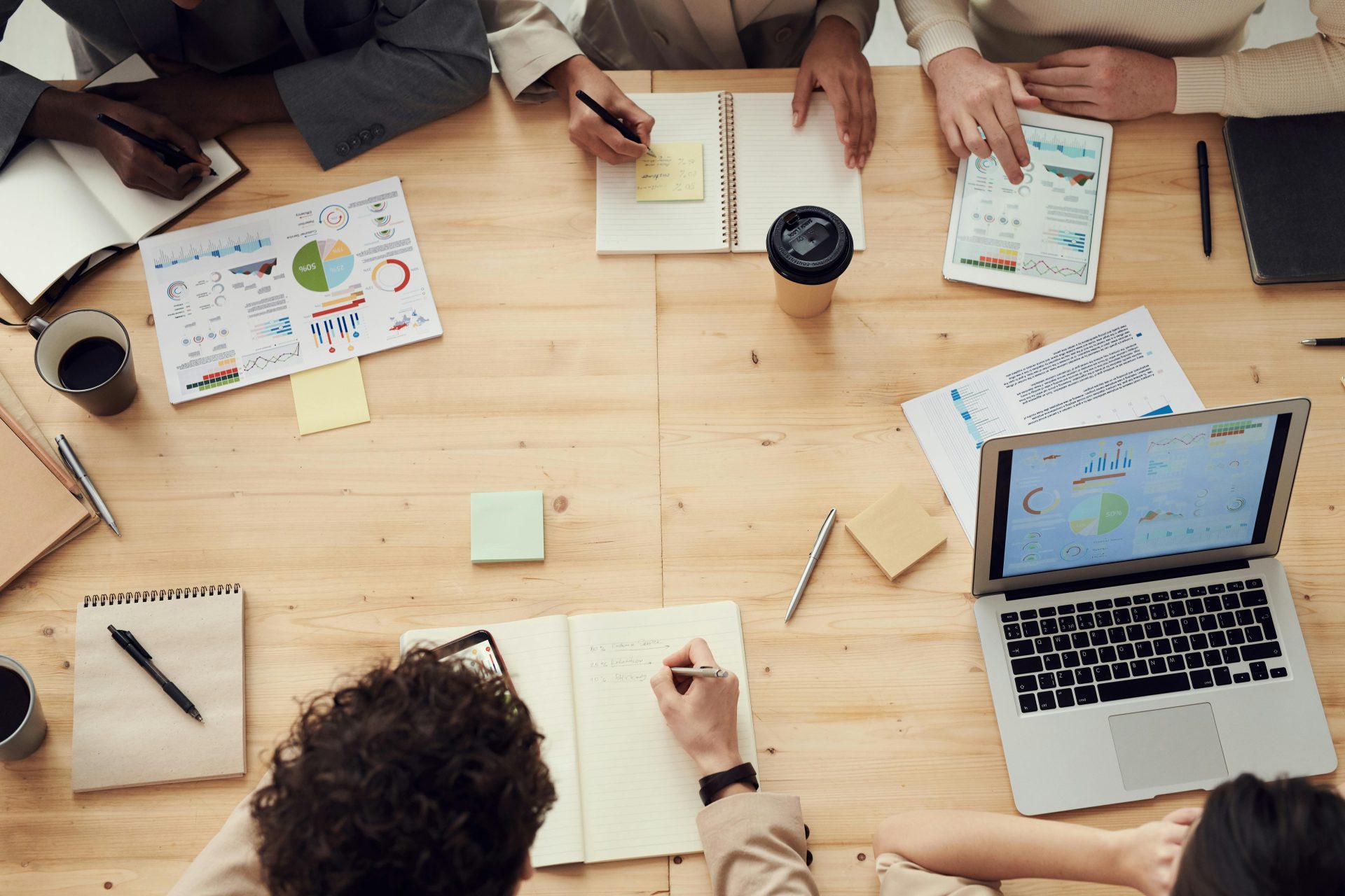 Geschäftsleute in einer gemeinsamen Teambesprechung, die Diagramme und Pläne mithilfe von Laptops und Notizbüchern besprechen.